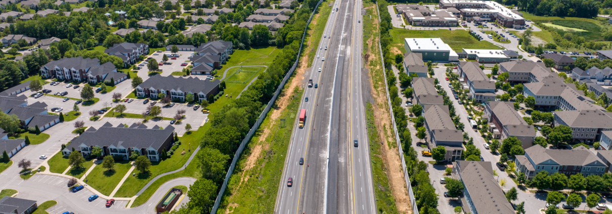 A drone photo of I-71. The highway has some cars on it. It cuts the picture in half. There are houses on either side of the highway.